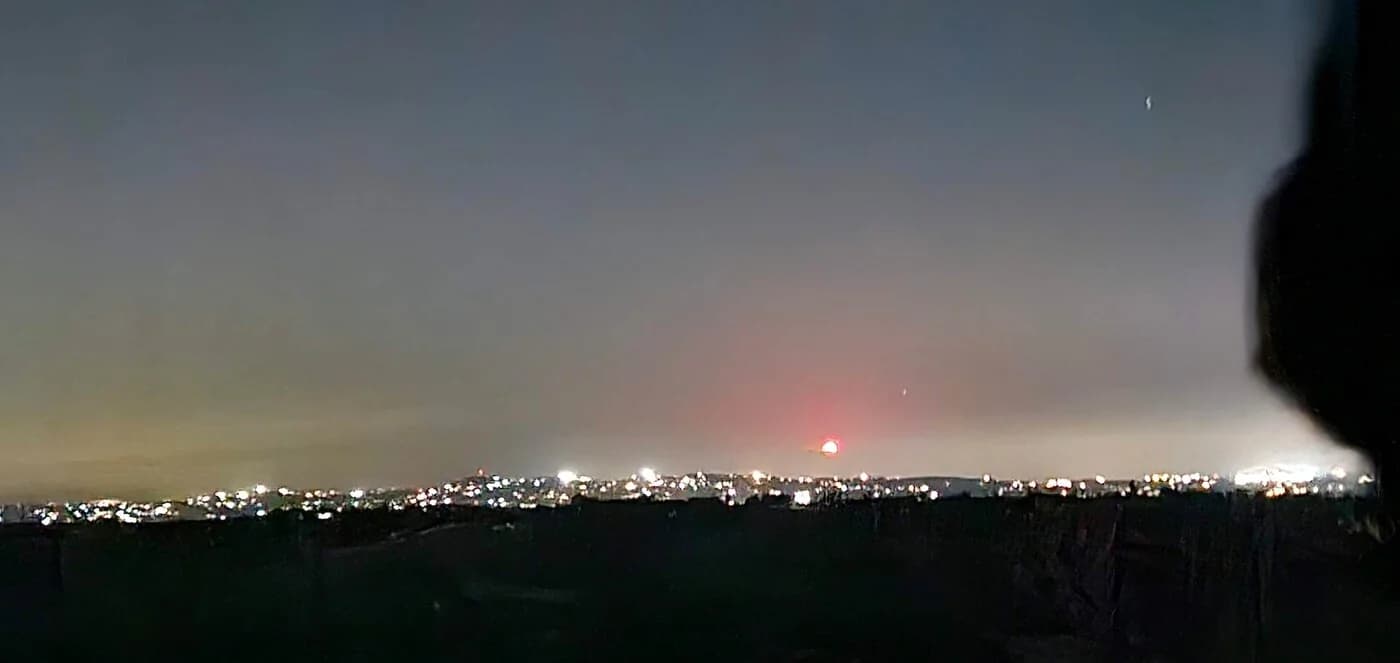 A town's lights on the horizon at night, seen from a dark hill