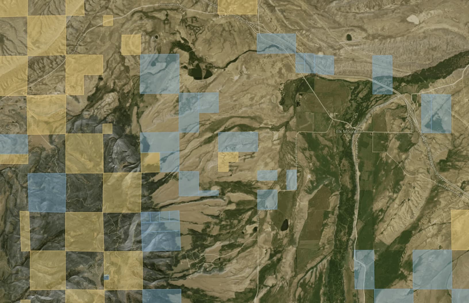 Satellite map of the checkerboard around Elk Mountain, Wyoming, in MapGridder with the Public Lands layer on: alternating yellow BLM squares and blue state trust squares, with the unshaded private squares of the ranch between them.